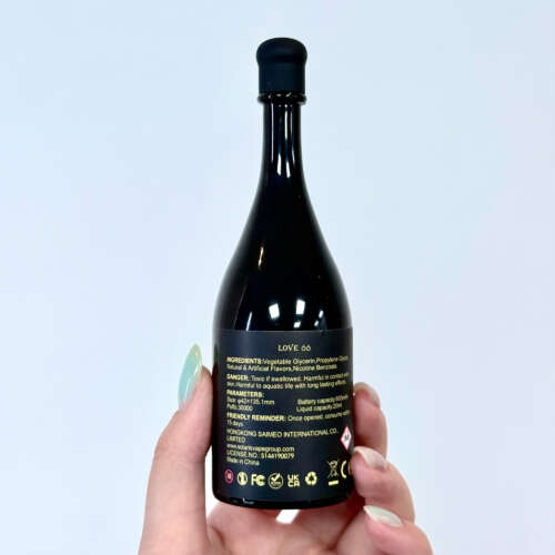 A person holds a black bottle labeled "LOVE 66," featuring ingredients and warnings on the back, with a sleek design and a pointed cap
