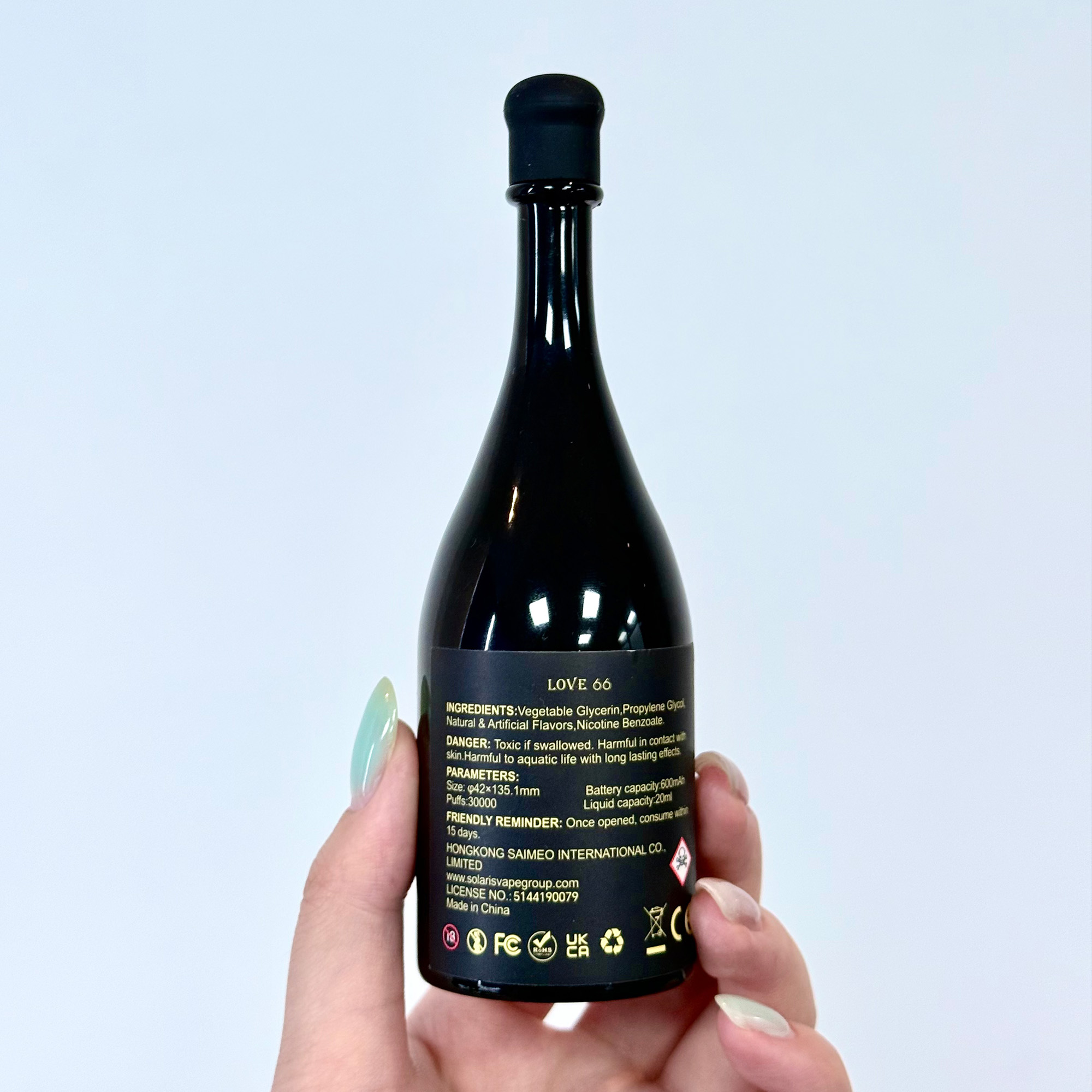 Iemand houdt een zwart flesje vast met het label "LOVE 66", met ingrediƫnten en waarschuwingen op de achterkant, en een strak ontwerp met een puntige dop